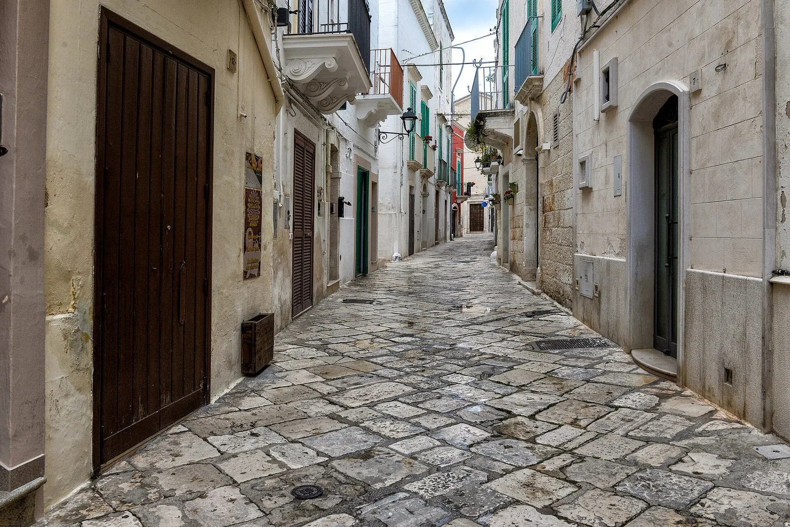 Vicolo lastricato del centro storico di Fasano fra le case in pietra e i balconi fioriti