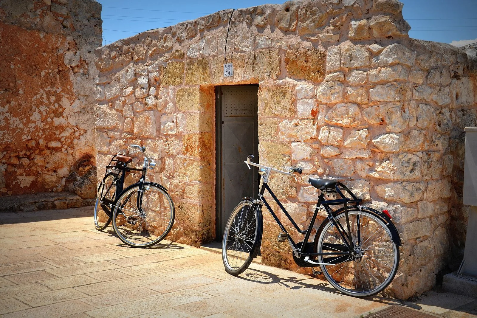 Due biciclette appoggiate a un muretto a secco in pietra lungo una strada di campagna pugliese