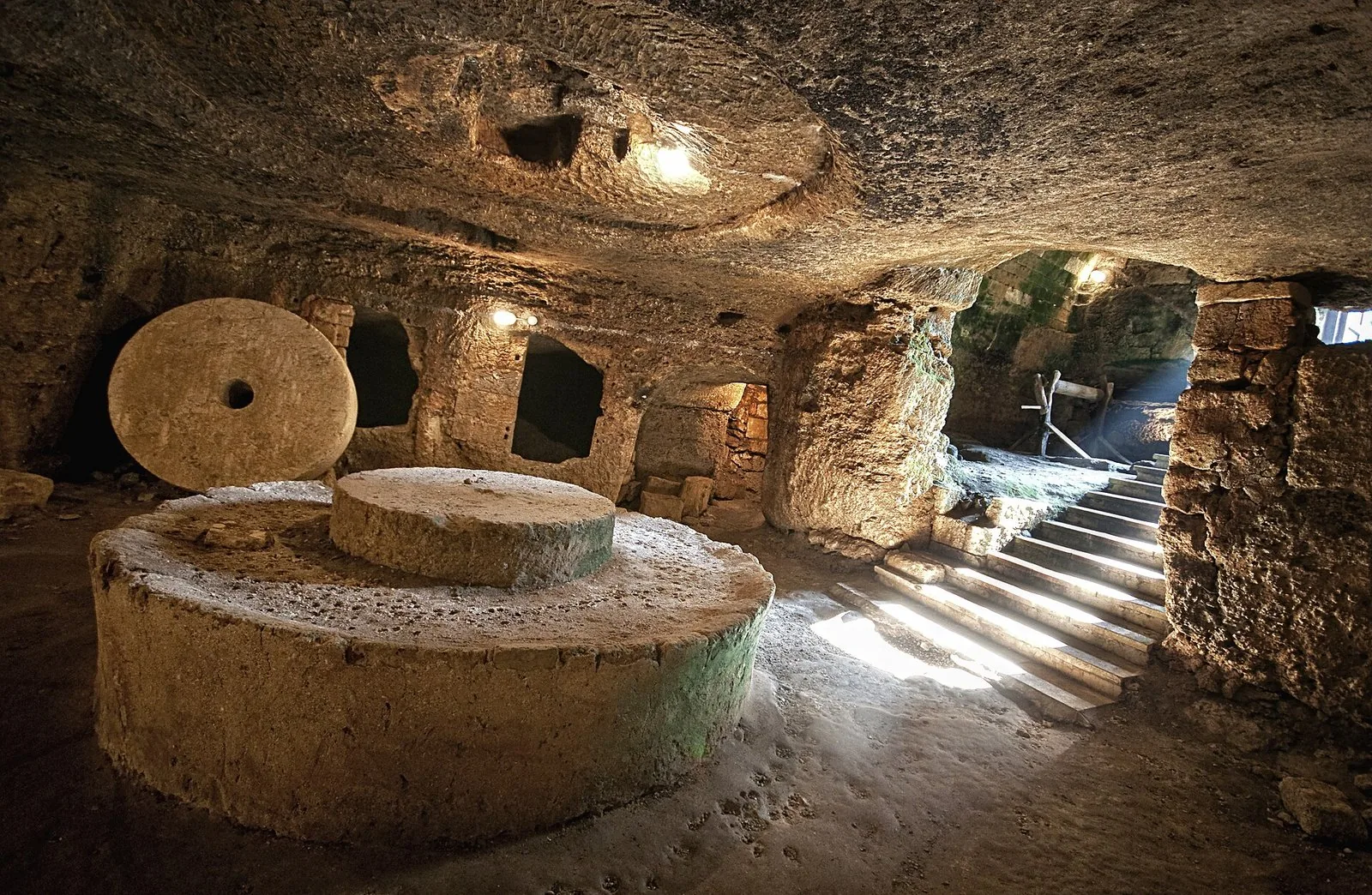 Interno di un frantoio ipogeo scavato nella roccia con l'antica macina in pietra per le olive